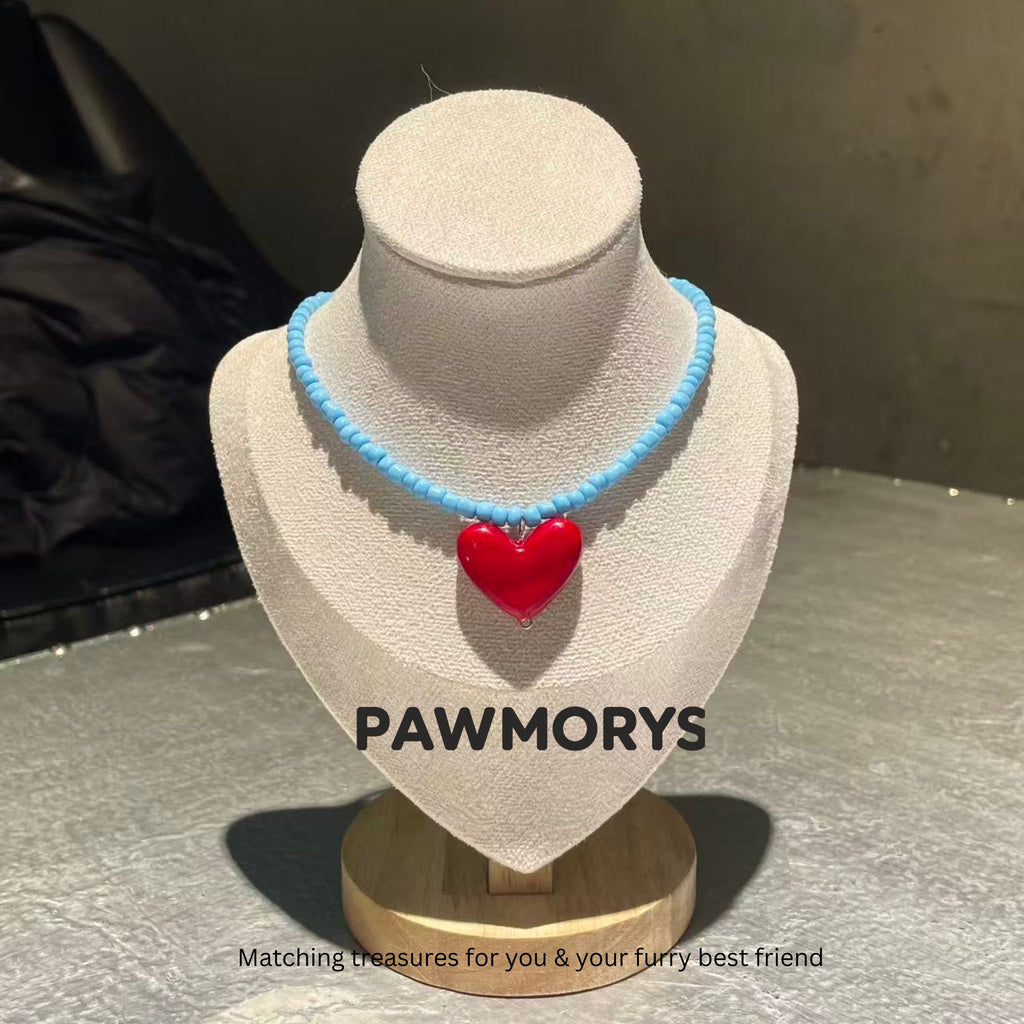 Sky-blue bead necklace with a glossy red heart pendant on a jewelry display