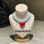 Sky-blue bead necklace with a glossy red heart pendant on a jewelry display