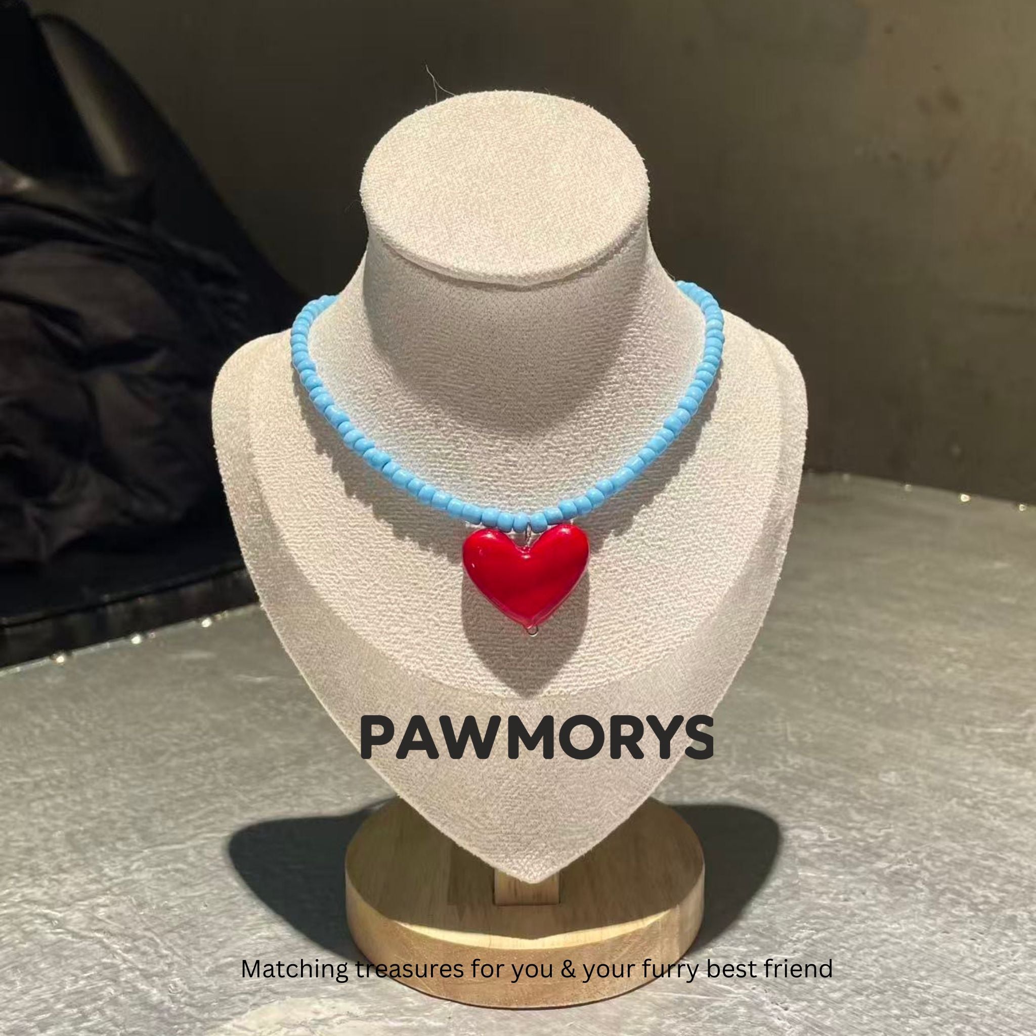 Sky-blue bead necklace with a glossy red heart pendant on a jewelry display