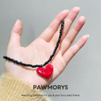 Black bead American Sweetheart necklace with a red heart pendant displayed by hand