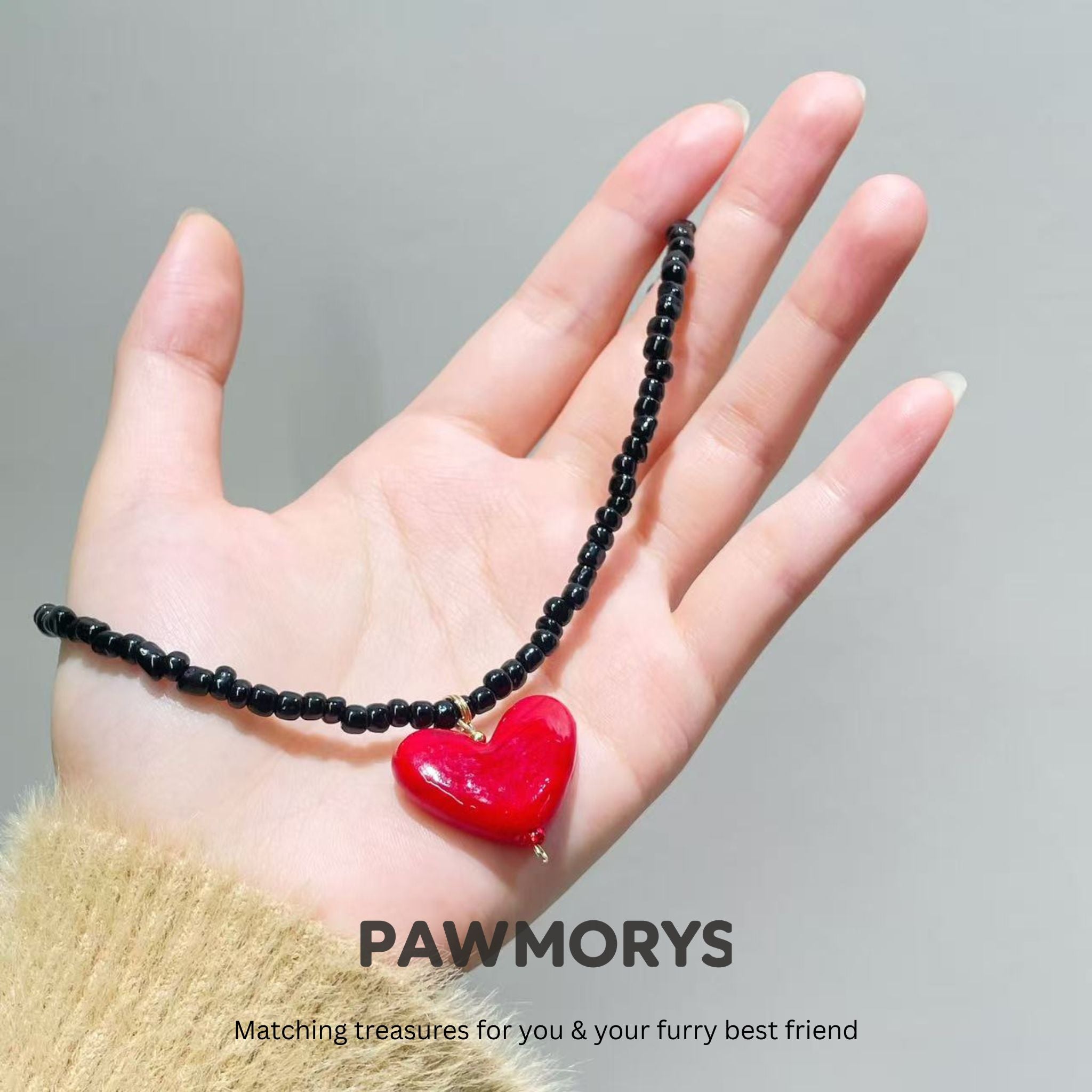 Black bead American Sweetheart necklace with a red heart pendant displayed by hand
